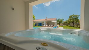 A hot tub with a control panel, a patio area with lounge chairs, and a view of a house with a red roof. - 3000sqm plot, with 50 sqm heated pool, jacuzzi, 2 tennis courts  (Marčana)