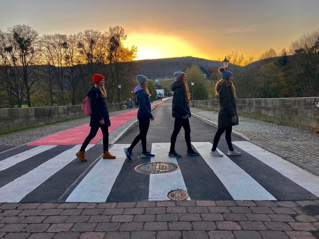 Quatro pessoas atravessando uma faixa de pedestres com o pôr do sol ao fundo.