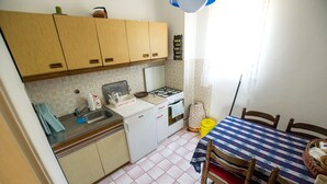 A compact kitchen with wooden cabinets, a gas stove, a sink, and a dining table with chairs. - Apartment with free Wi-Fi and air conditioning (Starigrad Paklenica)