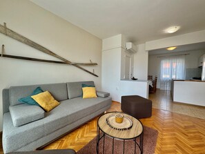 A modern living room with a grey sofa, a round coffee table, and a herringbone wooden floor.