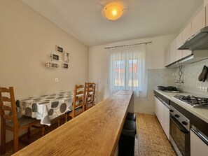 Ett kompakt kök med ett matbord, stolar, en spis och ett fönster med gardiner.