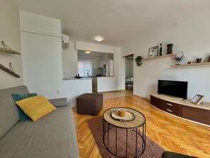 A modern living room with a grey sofa, a round coffee table, and a television on a wooden cabinet.