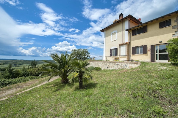 Una casa de dos pisos con base de piedra, un balcón y vistas al campo.