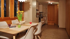 Un comedor con una mesa y sillas, un florero con flores y una cocina al fondo.