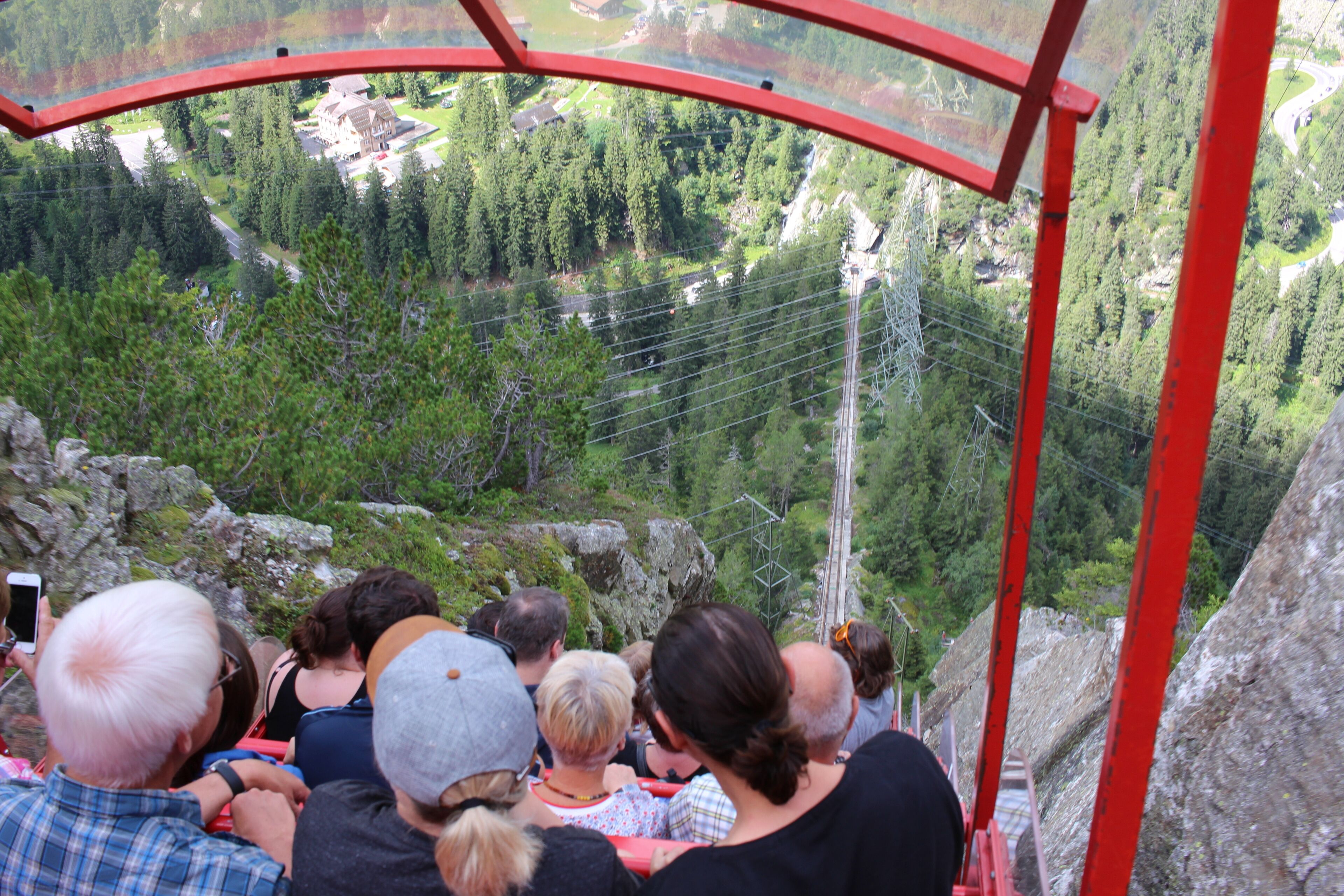 A group of people seated on a red metal structure overlooking a mountainous landscape with dense forests and power lines.