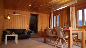 Un interior de madera con sofá, mesa de comedor, sillas y una mesita con lámpara.