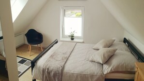 A bedroom with a sloped ceiling, a window with a view, a bed with striped bedding, and a chair.