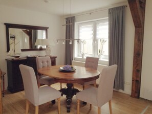 A dining area with a round wooden table, four upholstered chairs, a small decorative sailboat, and a mirror on the wall.