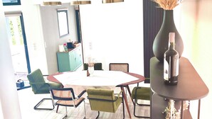 Et moderne spiseområde med et rundt bord, grønne polstrede stole og hængende pendellamper.
