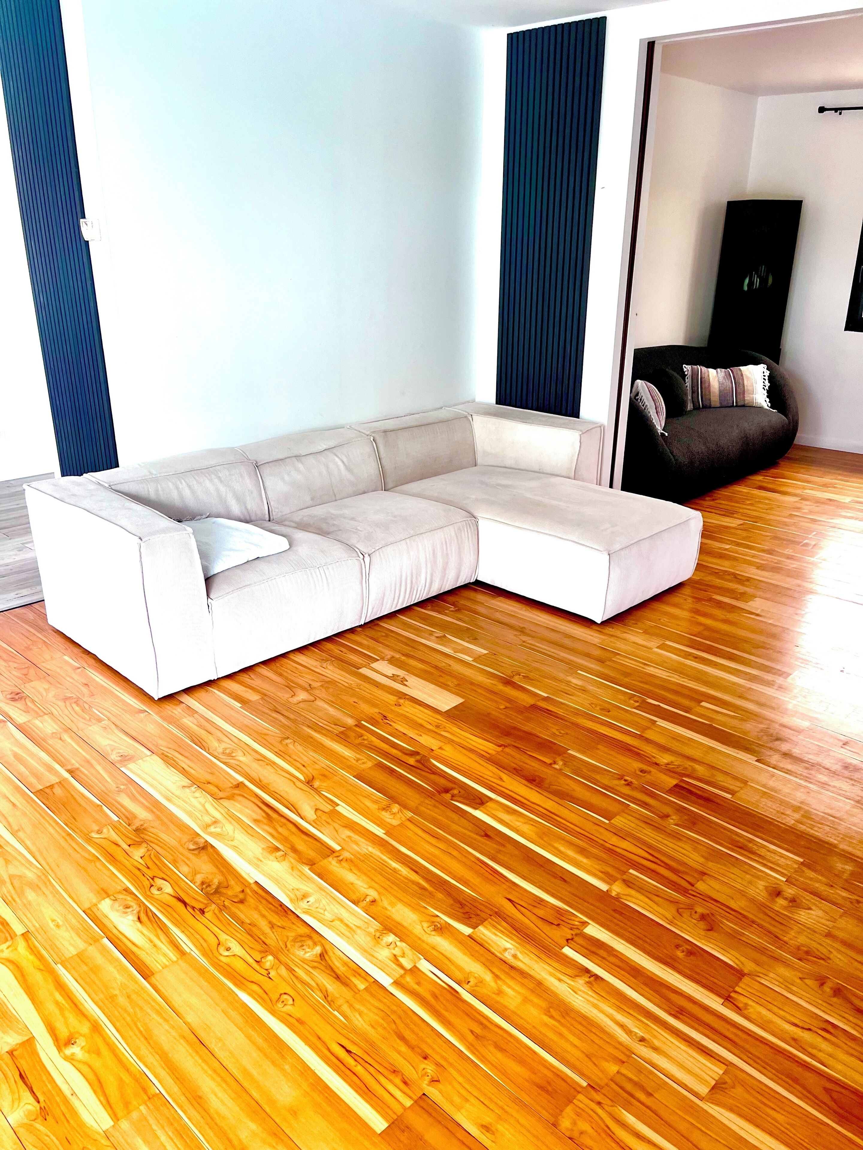 Una sala de estar con sofá modular, piso de madera y sillón oscuro.
