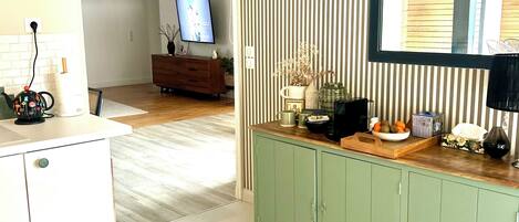 A modern kitchen with a green cabinet, a wooden countertop, and a television in the background.
