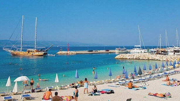 A beach with sun loungers and umbrellas, boats, and a rocky breakwater.