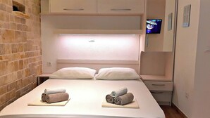 A hotel room with a bed, two pillows, a nightstand, a TV, and a brick wall.