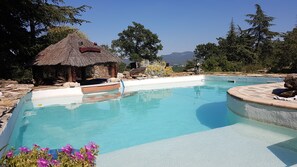 Una piscina con una cabaña de techo de paja, rodeada de rocas y árboles.