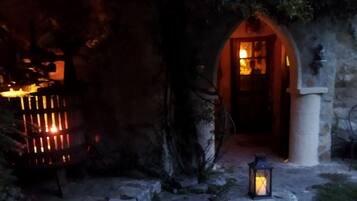 A stone pathway leading to a rustic building with a wooden door and a lantern.
