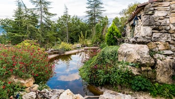 Un edificio de piedra con un estanque, rodeado de árboles y plantas con flores.