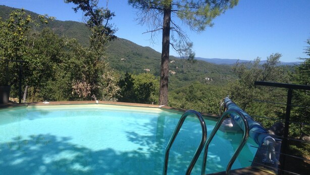 Una piscina con cubierta de madera y barandillas metálicas, rodeada de árboles y colinas.