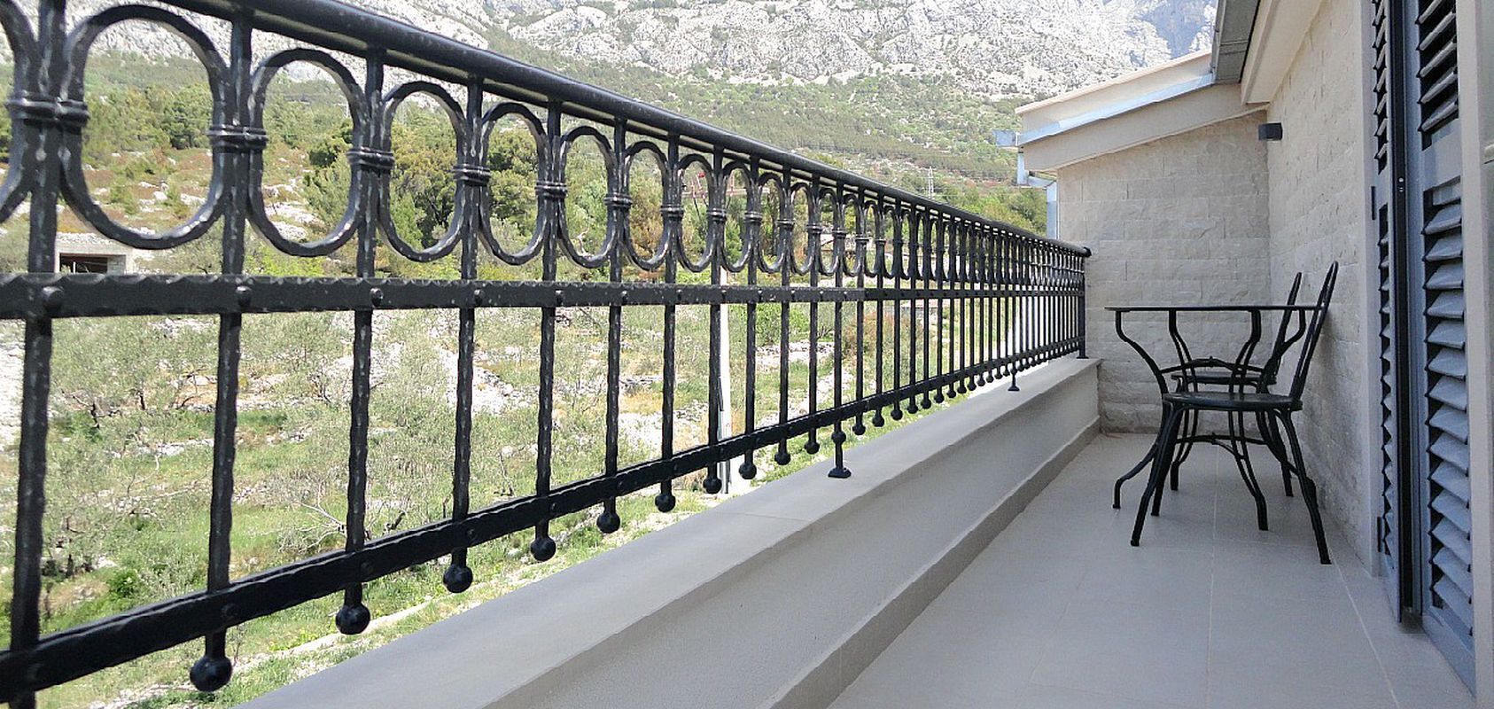 Un balcon avec une balustrade en fer forgé, une petite table et deux chaises.