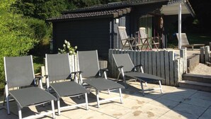 Une terrasse avec quatre chaises longues et un petit bâtiment doté d’un toit en tuiles.