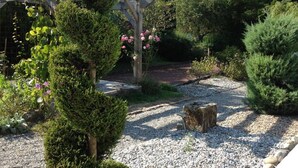 Un jardin avec un chemin de gravier, une pergola en bois et divers arbustes et fleurs.