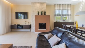 A modern living room with a black leather sofa, a flat-screen TV mounted on the wall, a fireplace, and a dining area with a table and chairs. - Luxury villa with heated pool by the sea in a quiet area (Pula - Pomer)