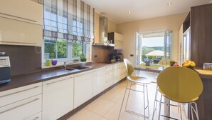 A modern kitchen with white cabinets, a built-in stove, and a window with blinds. - Luxury villa with heated pool by the sea in a quiet area (Pula - Pomer)