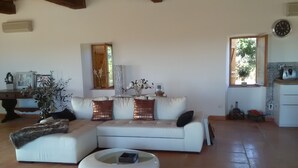 A spacious living area with a white sofa, a coffee table, and a dining area with a kitchen counter.