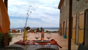 An outdoor dining area with a table set for two, a bottle of wine, and a view of the sea.