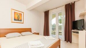 Habitación de hotel con cama, escritorio con televisor, un cuadro en la pared y vistas al exterior a través de una puerta corrediza.