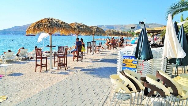 Zona de playa con sombrillas de techo de paja, sillas de descanso y piscina.