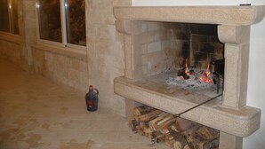 Una chimenea de piedra con fuego encendido, un ventanal con vistas y una botella de combustible en el suelo.
