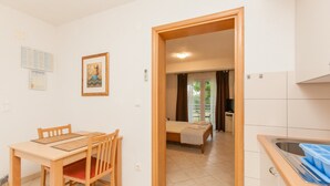 Una habitación con una mesa de comedor de madera, una cama con colcha a cuadros, una kitchenette con un lavaplatos y una puerta que da a otra habitación.