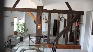 A spacious room with exposed wooden beams, a dining area with a glass table, and a potted plant.
