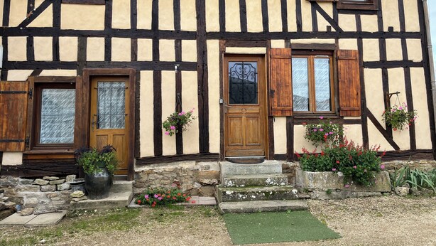 A traditional half-timbered house with a stone foundation, wooden doors, and windows with shutters.