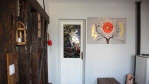 A wooden door with a glass panel, a framed artwork of a tree with a red sun, and a small wooden chest.