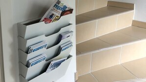 A staircase with beige tiles and a wall-mounted magazine rack with various papers.