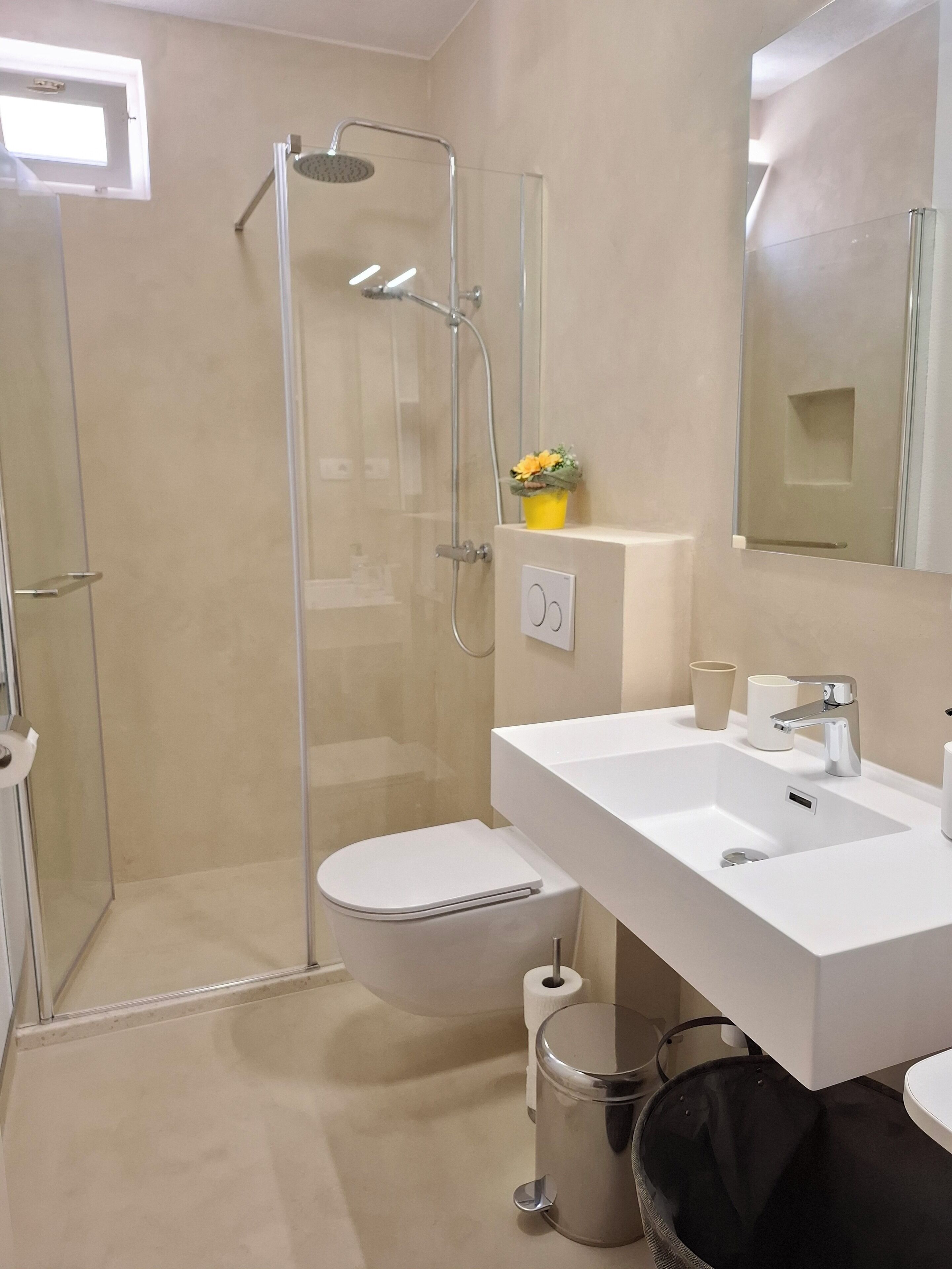 Een moderne badkamer met een douche met glazen wand, een wit toilet en een witte wastafel met een spiegel erboven.