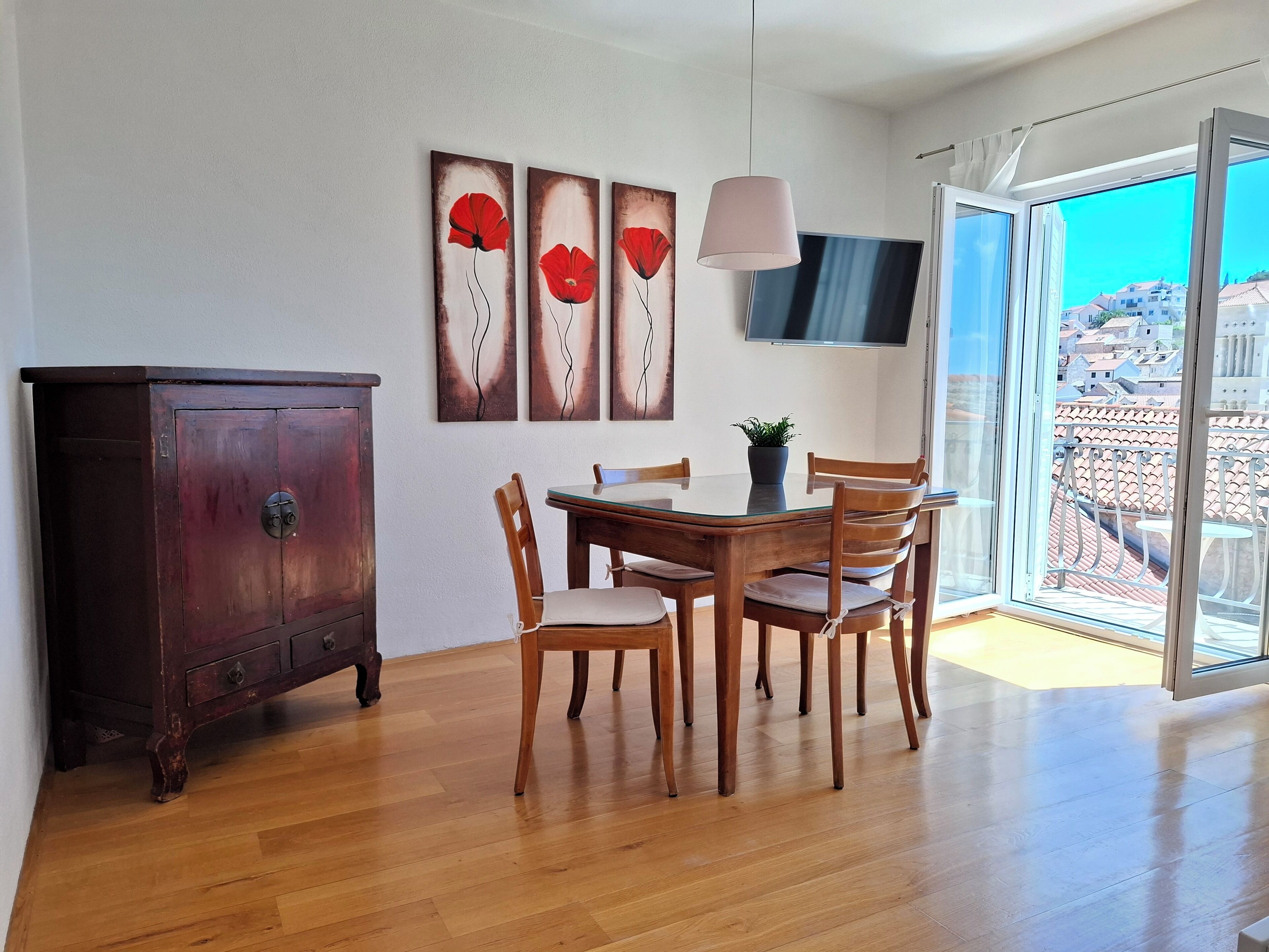 Een eetgedeelte met een houten tafel, stoelen, een kast en een aan de muur bevestigde televisie.