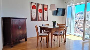 Een eetgedeelte met een houten tafel, stoelen, een kast en een aan de muur bevestigde televisie.
