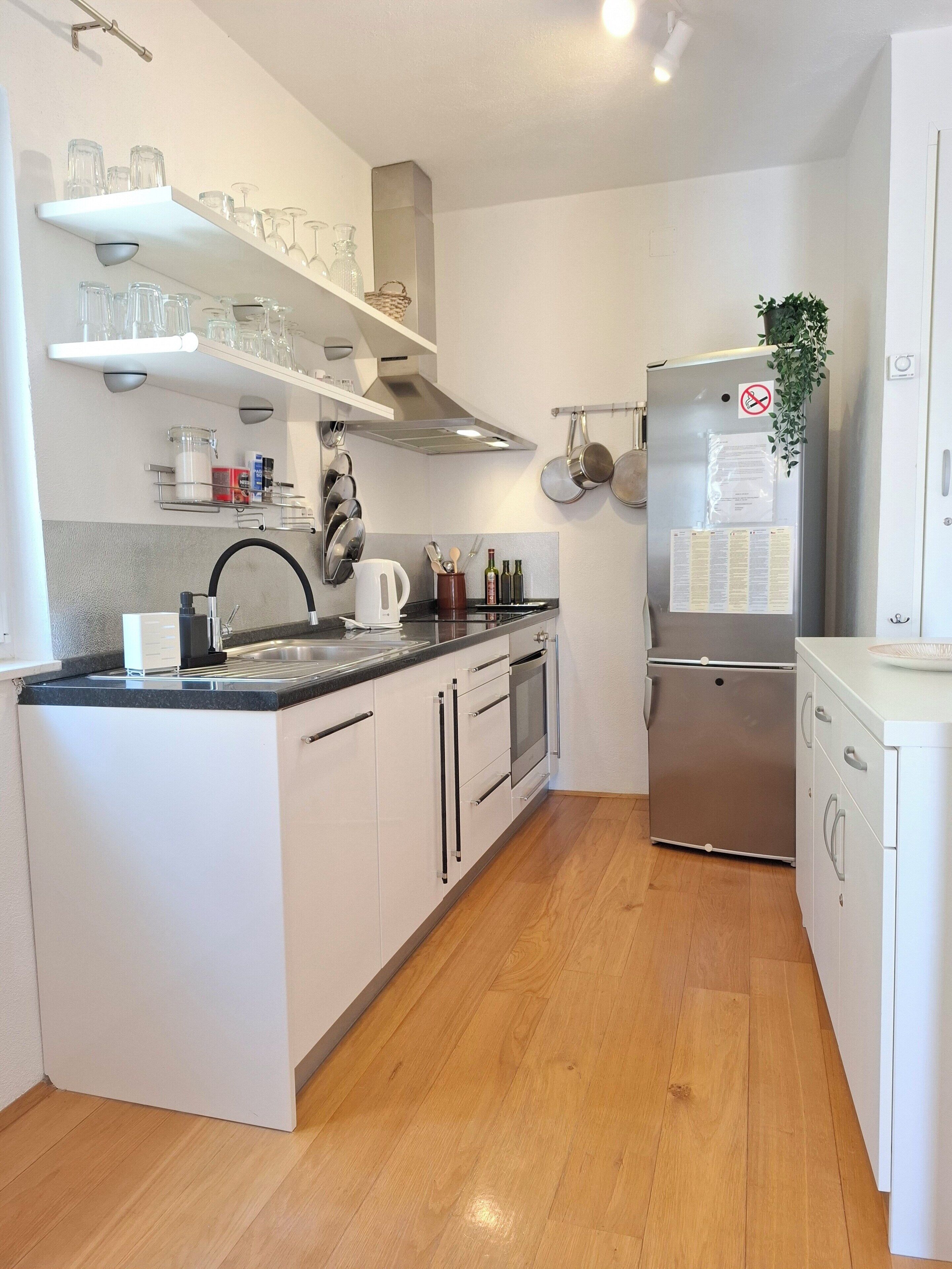 A modern kitchen with white cabinets, a stainless steel refrigerator, and a wooden floor.