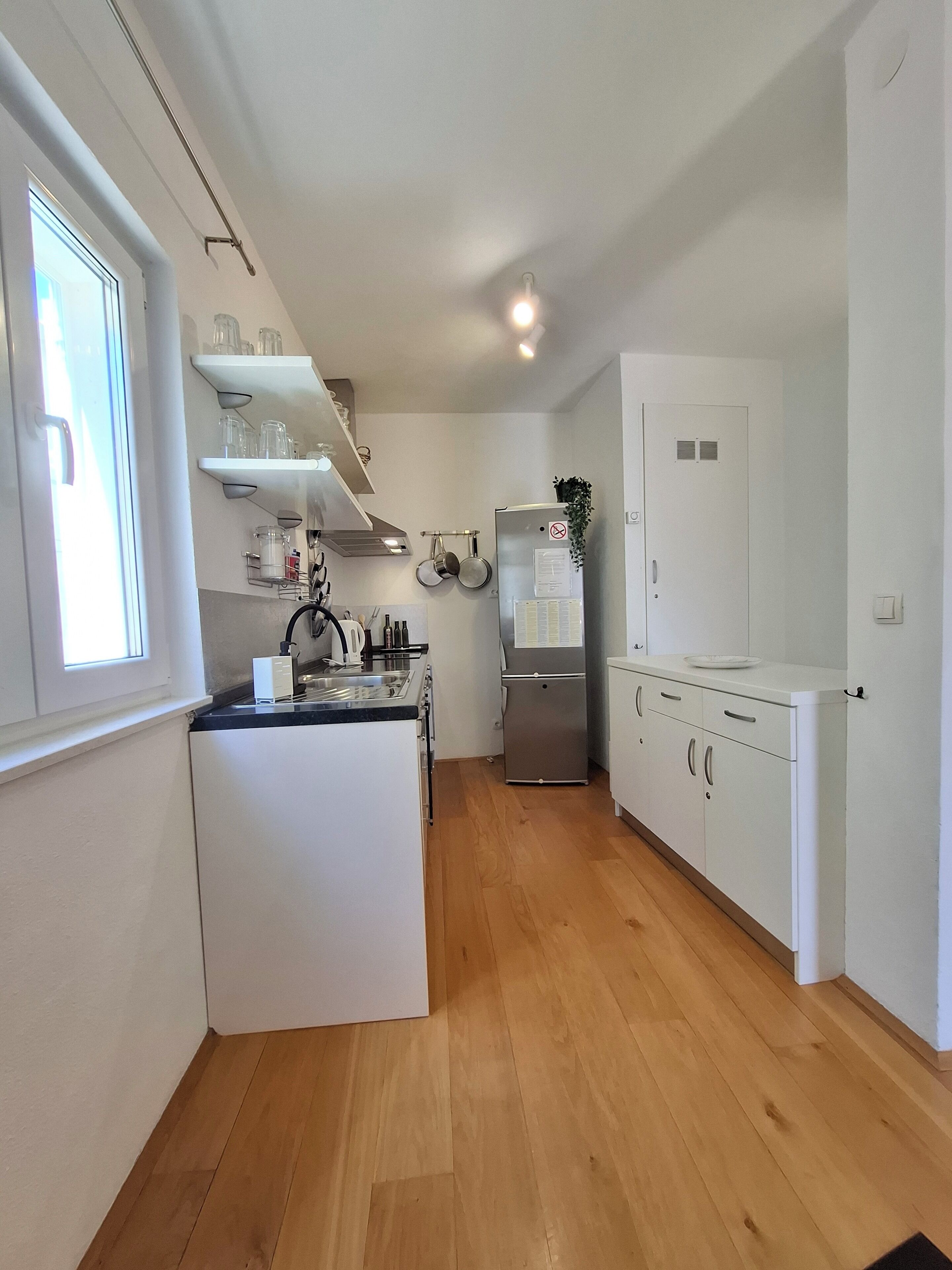 A compact kitchen with white cabinetry, a stainless steel refrigerator, and wooden flooring.