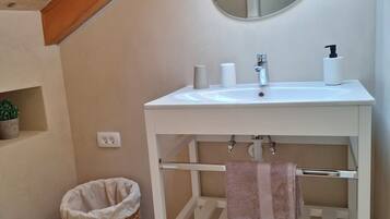 Et badeværelse med et hvidt toiletbord, et rundt spejl, en håndklædestang og en lille kurv af fletværk.