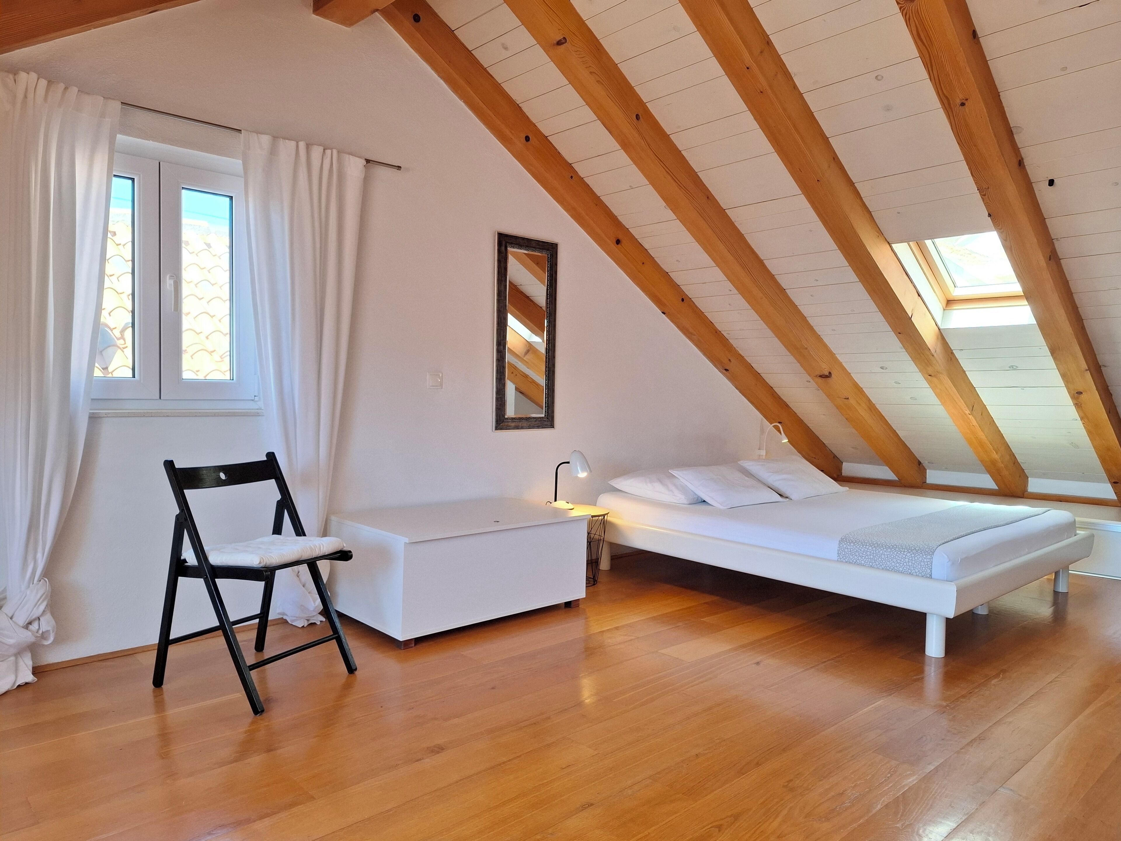 Une chambre avec un plafond de style industriel, un lit, une chaise et une table de chevet.