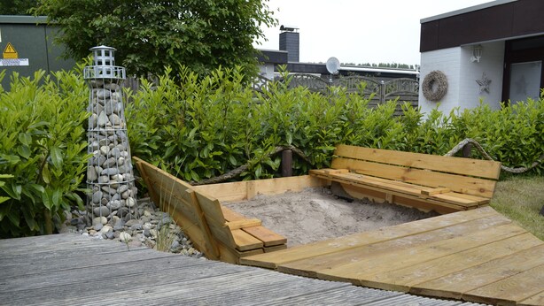 Eine Holzterrasse mit Sitzgelegenheit und einem Steingebäude.
