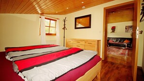 Ein Schlafzimmer mit einem großen Bett, einem Holzkopfteil, einem Kleiderständer und einer Tür zu einem Wohnbereich mit einer Couch und einem Teppich.