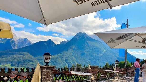 Ein Essbereich im Freien mit Tischen und Stühlen, vor einer Berglandschaft.