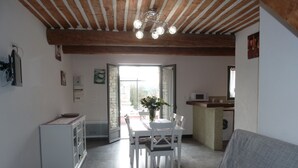 A modern kitchen with a dining area, a sofa, and a view through an open door. - Charming stone cottage -air conditioner. Shared pool with 2 houses 10x5 m (Gordes)
