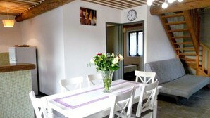 A dining area with a white table and chairs, a vase with flowers, a clock on the wall, and a staircase. - Charming stone cottage -air conditioner. Shared pool with 2 houses 10x5 m (Gordes)