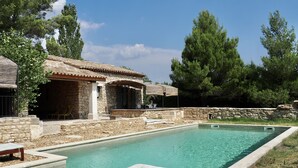 A pool area with a lounge chair, a stone building with a tiled roof, and surrounding greenery. - Charming stone cottage -air conditioner. Shared pool with 2 houses 10x5 m (Gordes)