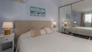 Une chambre à coucher avec un grand lit, deux tables de chevet avec des lampes, un climatiseur fixé au mur et un tableau représentant un bateau accroché au mur.